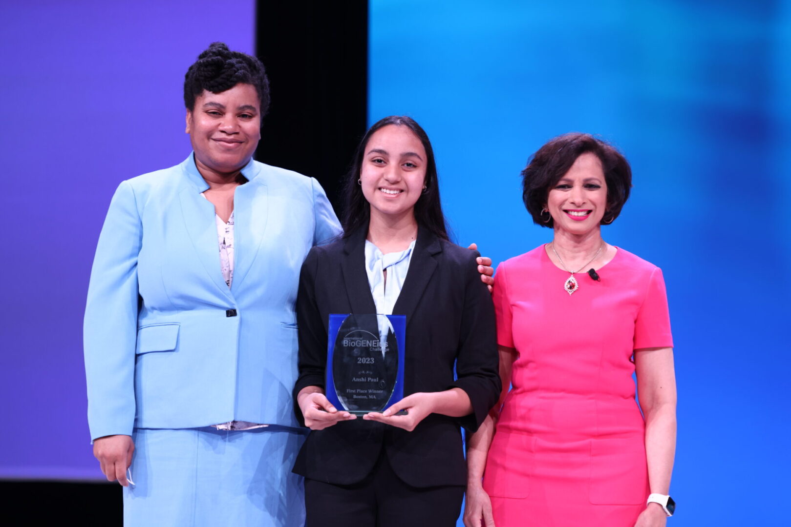 Three women stand together, one holding an award.