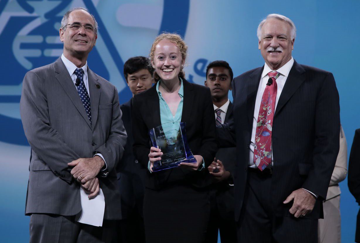 Group of professionals at an award ceremony with a woman holding a trophy.
