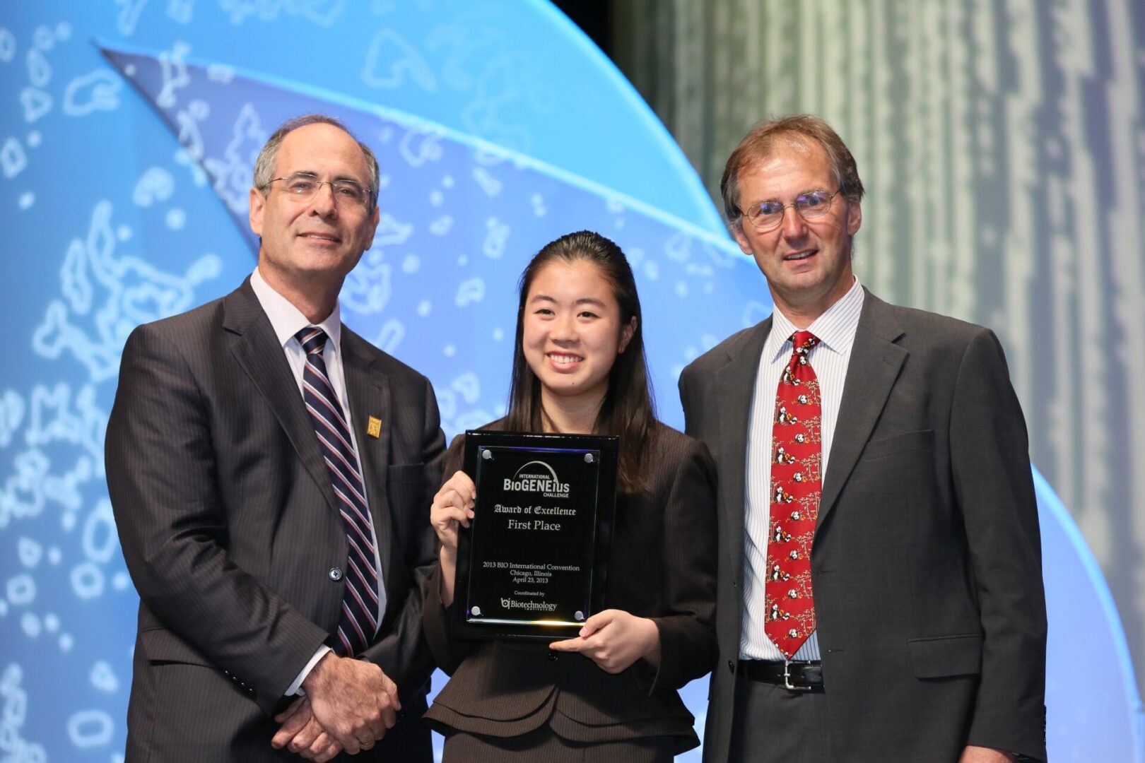 Three people at an award ceremony, woman in center holding a plaque.