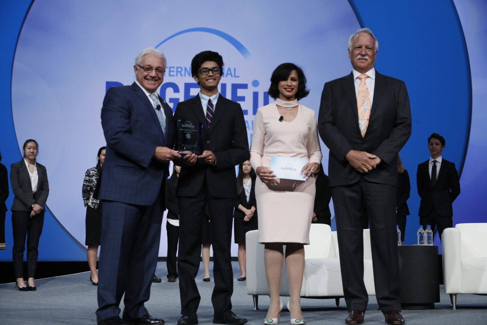 Four formally dressed individuals stand on stage in front of a GEF logo.