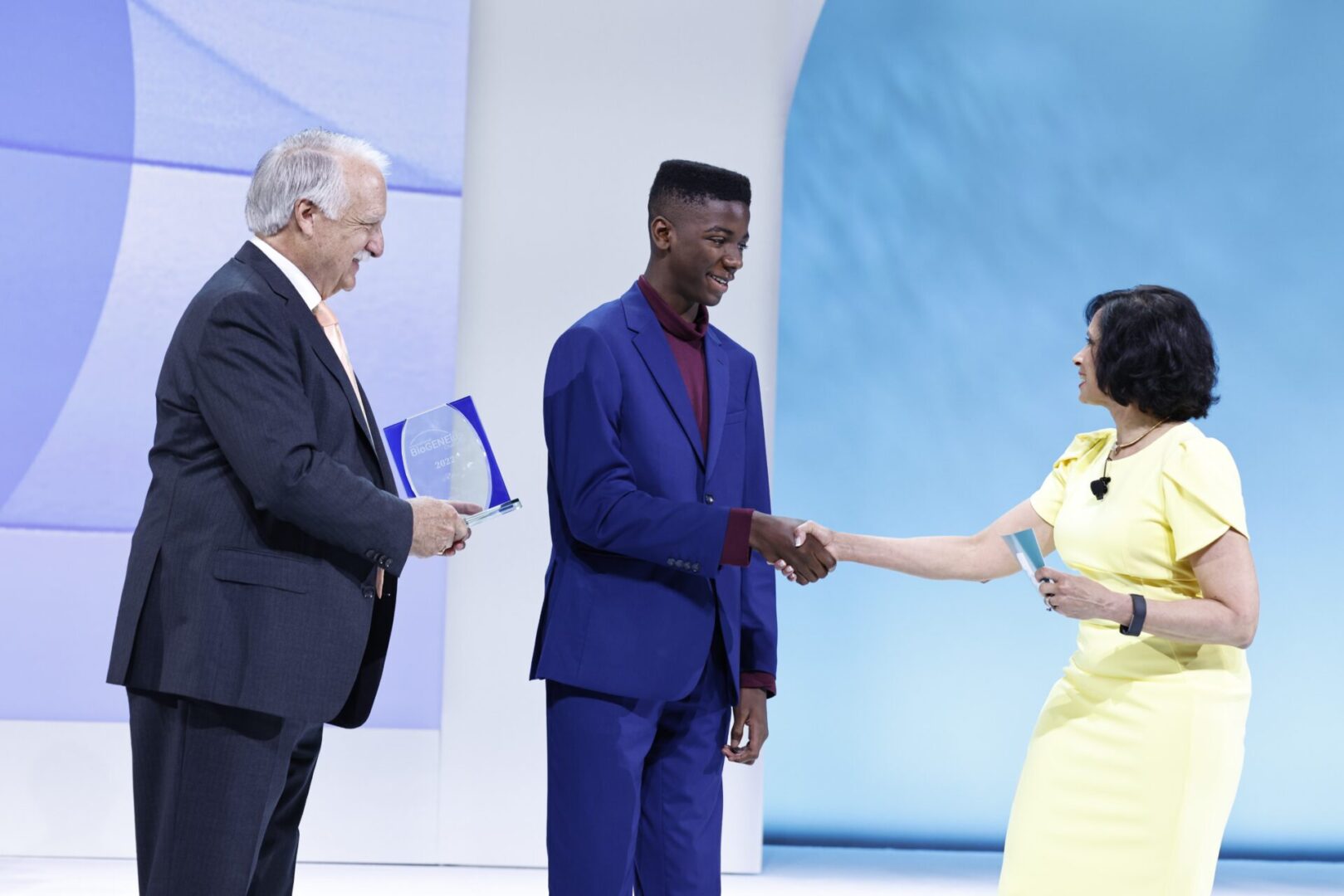 Man in blue suit receiving award and shaking hands with woman.