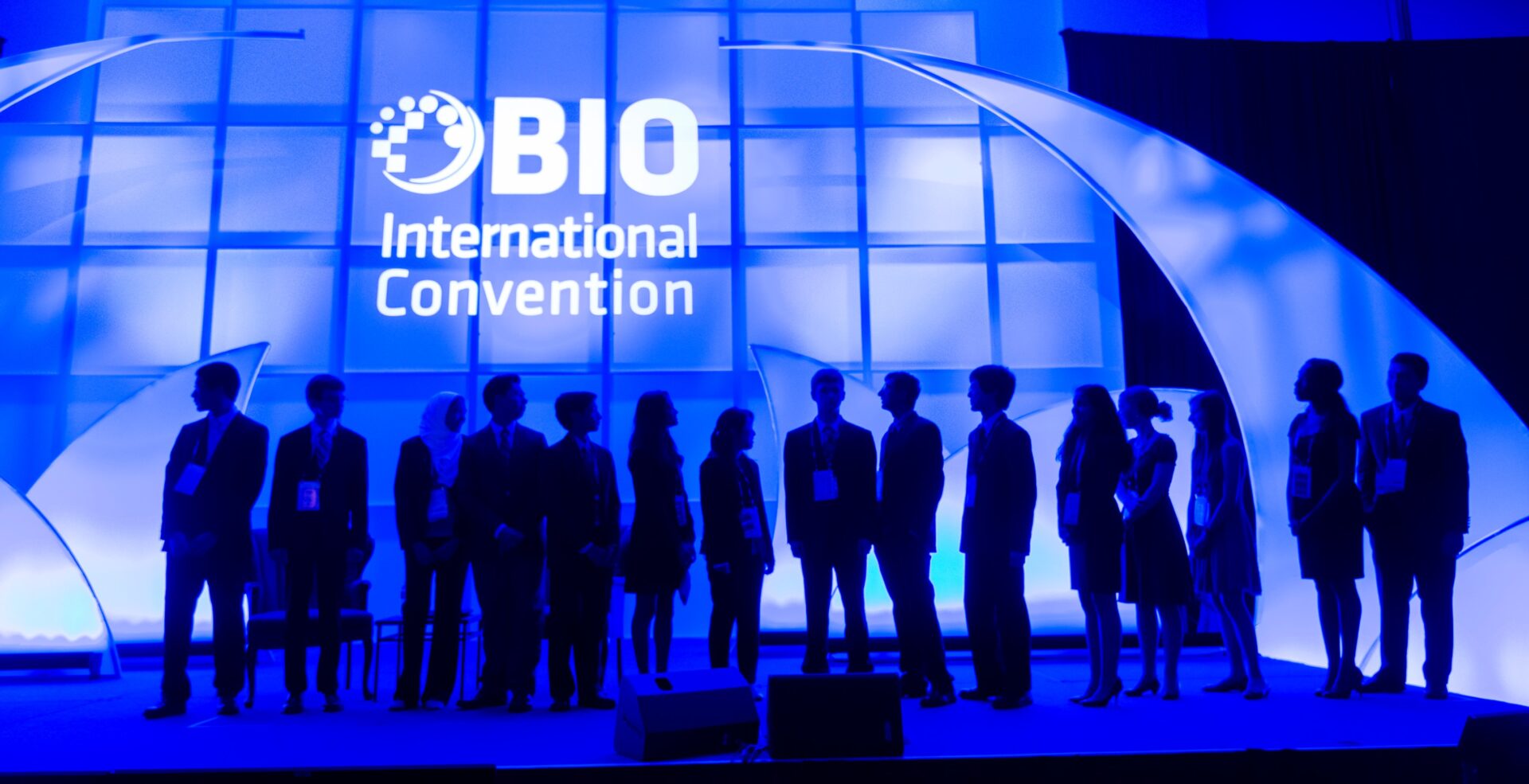 Silhouetted group at OBIO International Convention stage with blue lighting.